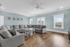 A spacious living room with a sectional sofa, a coffee table, and a ceiling fan. - Sea Y'all Soon - Oceanfront in Garden City Beach (Garden City Beach)