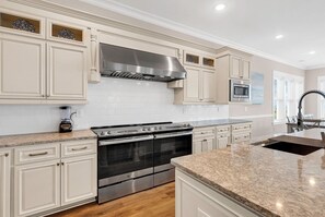 A modern kitchen with white cabinetry, stainless steel appliances, and a granite countertop. - Sea Y'all Soon - Oceanfront in Garden City Beach (Garden City Beach)