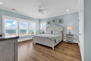 A bedroom with a bed, two bedside tables, a ceiling fan, and a view of the ocean through large windows. - Sea Y'all Soon - Oceanfront in Garden City Beach (Garden City Beach)