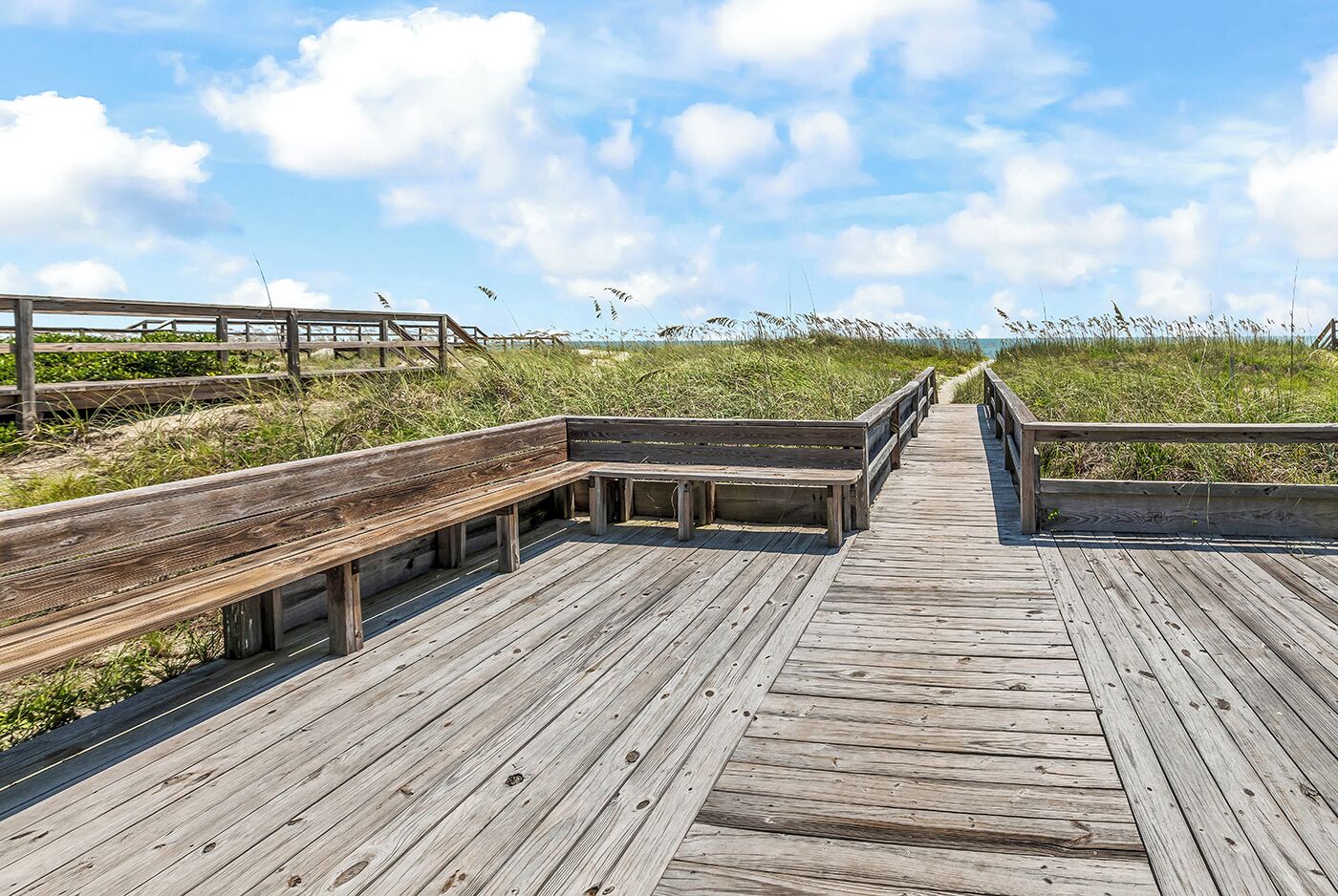 A wooden boardwalk leading to a beach with benches and railings.