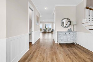 A hallway with a white wainscotted wall, a white dresser with drawers, and a round mirror on the wall. - Sea Y'all Soon - Oceanfront in Garden City Beach (Garden City Beach)