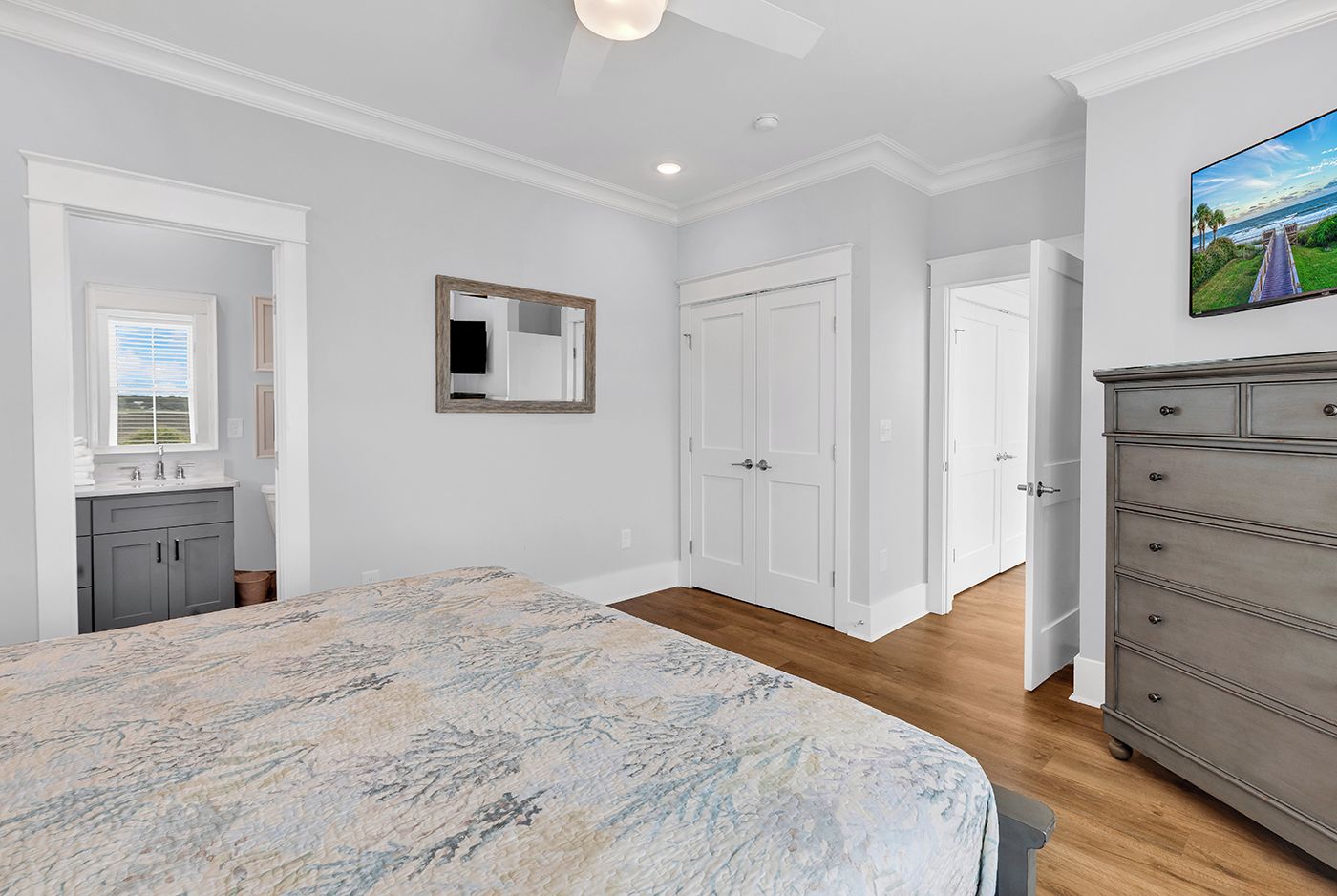A bedroom with a bed, a dresser, a mirror, and a door leading to another room.