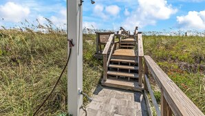 A wooden staircase leading to a wooden platform with a metal railing, surrounded by grass and wildflowers. - Y'all Have Fun - Oceanfront in Garden City Beach (Garden City Beach)