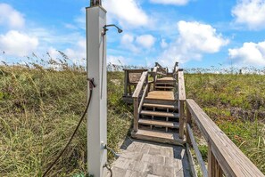 Eine Holztreppe führt zu einer Holzplattform mit einem Metallgeländer, umgeben von Gras und Wildblumen.