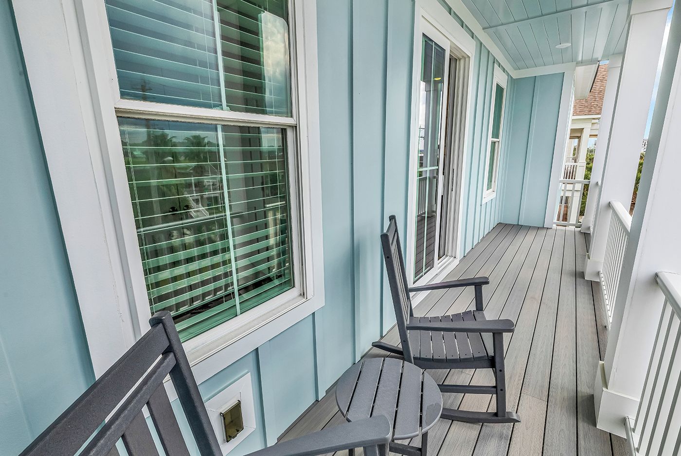 A covered porch with a bench and a table, a window with blinds, and a white railing.
