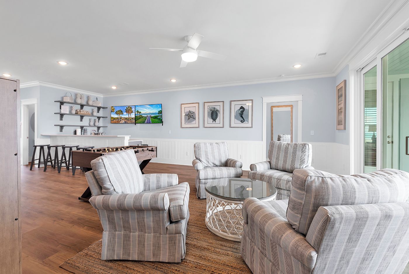 A spacious living room with a wooden floor, a glass coffee table, and striped armchairs.