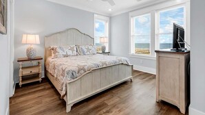 A bedroom with a wooden bed, two bedside tables with lamps, a ceiling fan, and a TV on a stand. - Y'all Have Fun - Oceanfront in Garden City Beach (Garden City Beach)