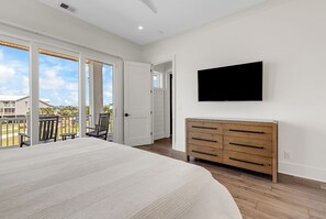 A bedroom with a large bed, a TV mounted on the wall, and a wooden dresser. - Coastal Point of View 10 Bedroom - Oceanfront in Garden City Beach (Garden City Beach)