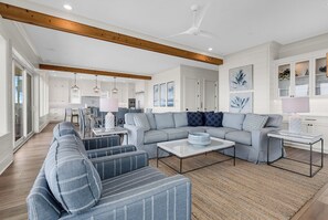A spacious living room with a grey sofa set, a coffee table, and a dining area with a chandelier. - Coastal Point of View 10 Bedroom - Oceanfront in Garden City Beach (Garden City Beach)