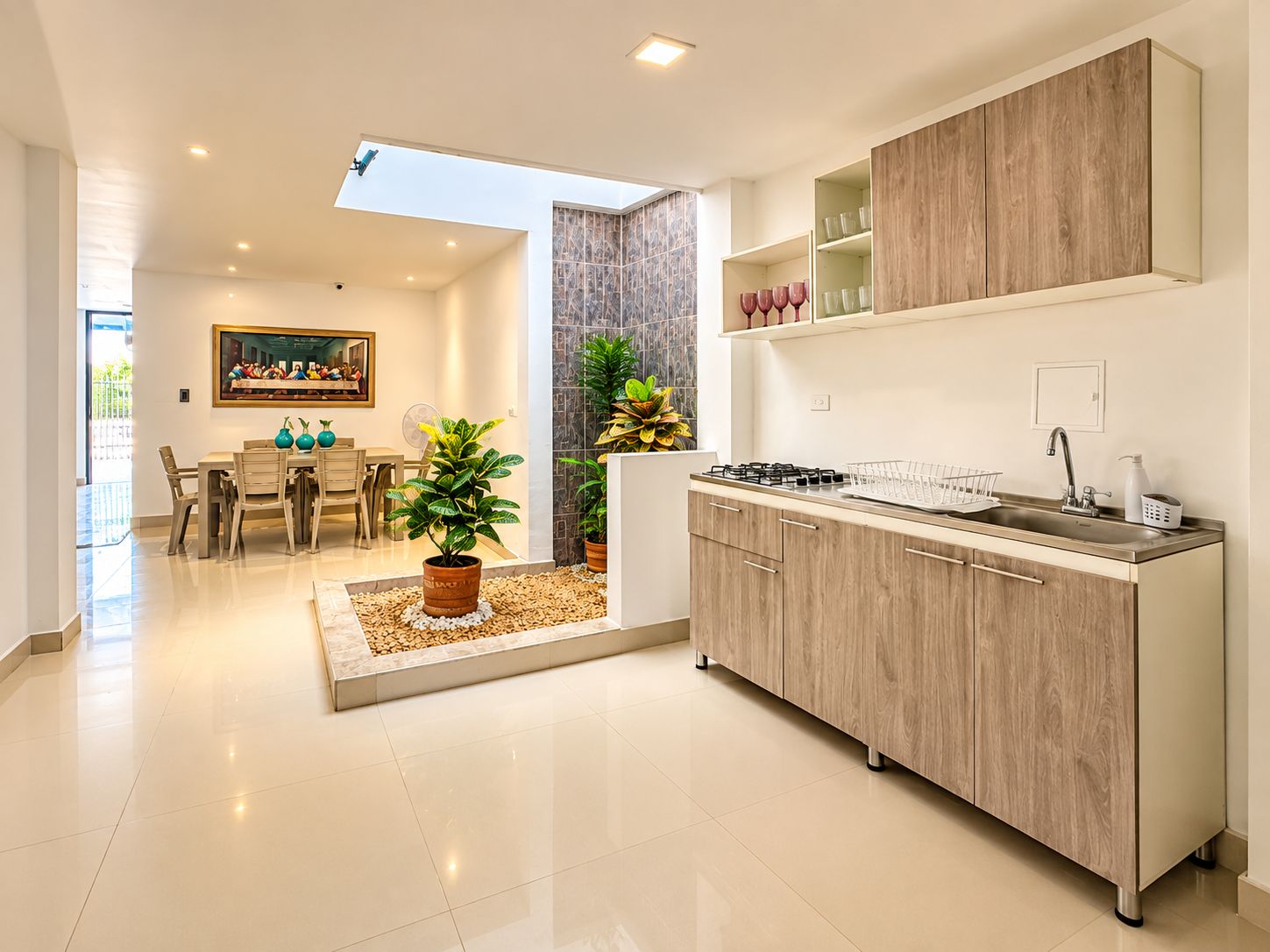 A modern kitchen with a skylight, a dining area with a painting, and a potted plant.