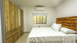 A bedroom with a bed, wooden wardrobe, window, and air conditioning unit.