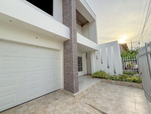 Une maison moderne à deux étages, dotée d’une porte de garage blanche, d’un pilier en pierre et d’une terrasse carrelée.