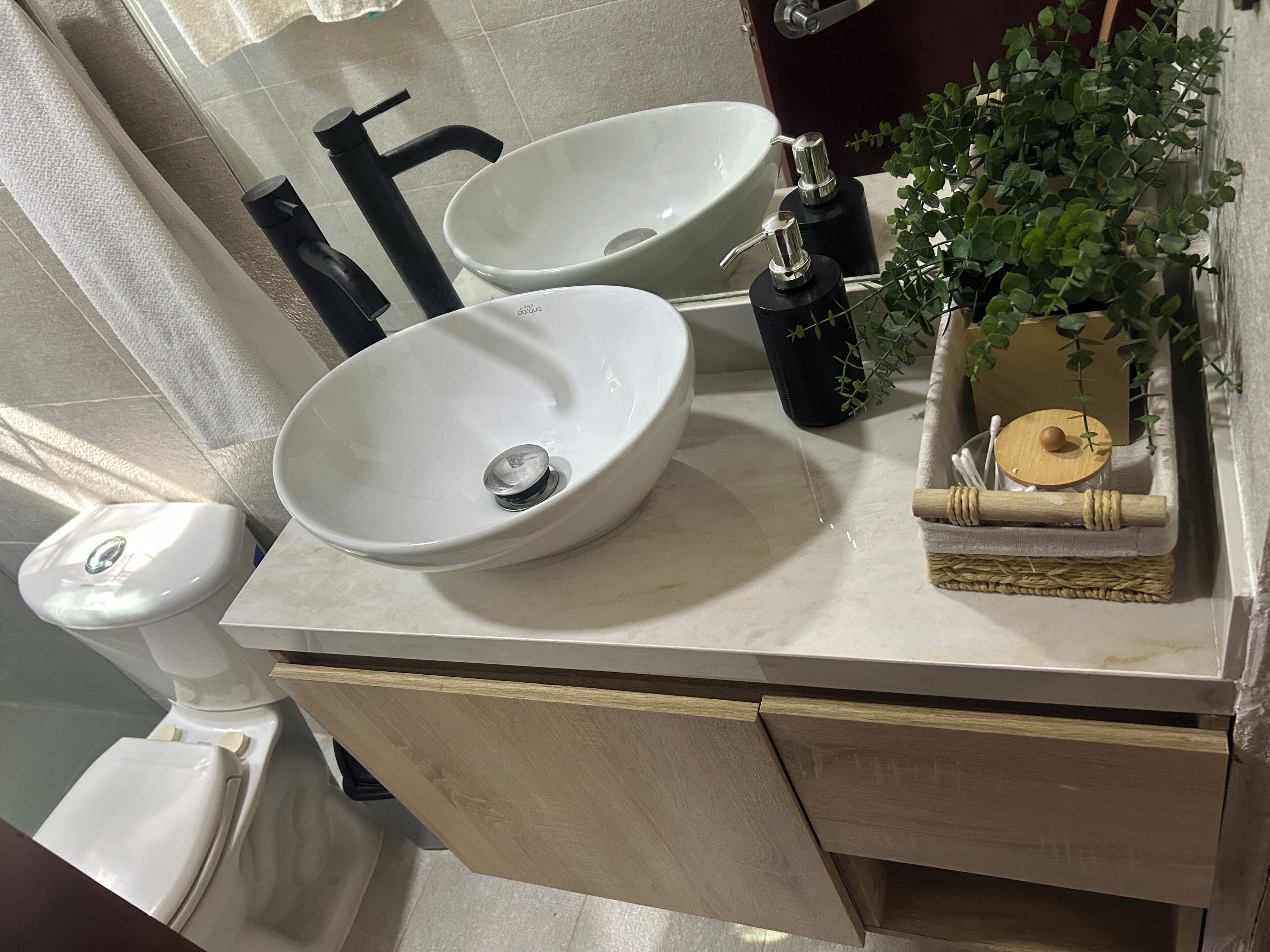 A bathroom with two white sinks, a toilet, and a small plant on the counter.