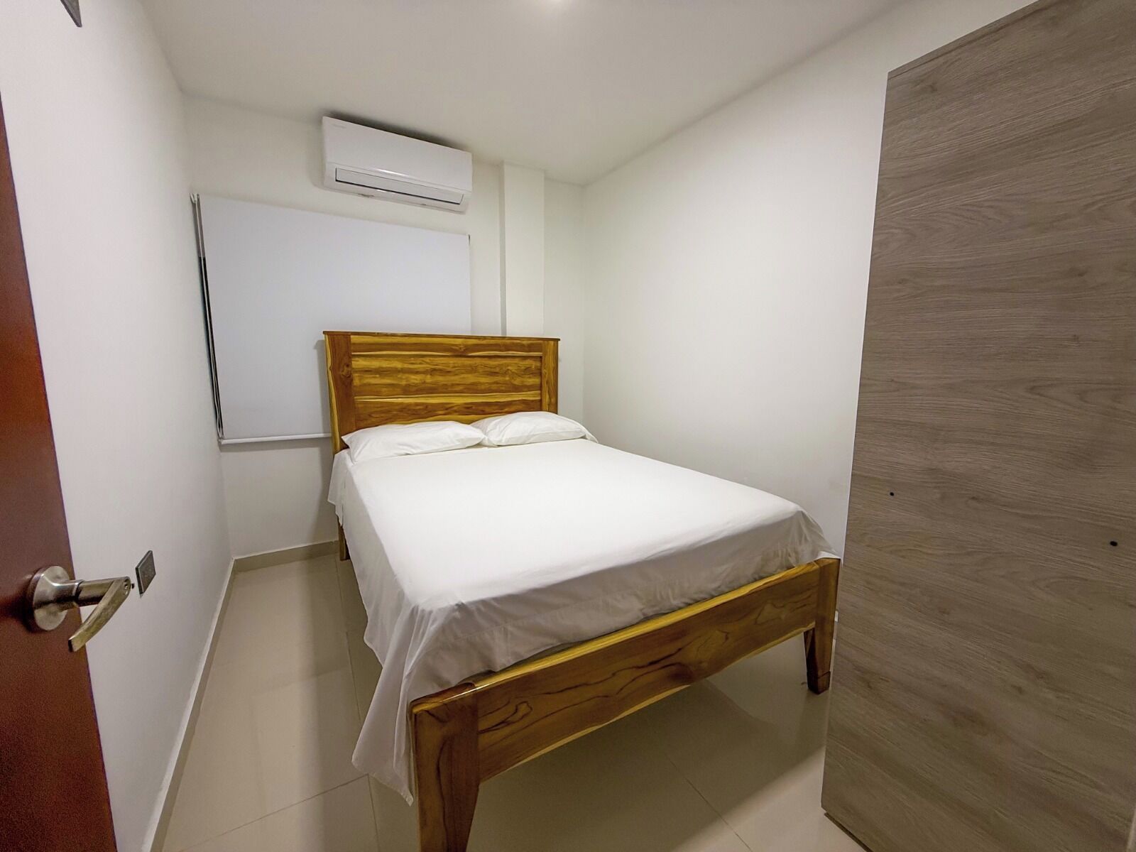 A single bed with a wooden headboard in a room with white walls and a wooden door.