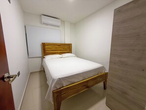 A single bed with a wooden headboard in a room with white walls and a wooden door.