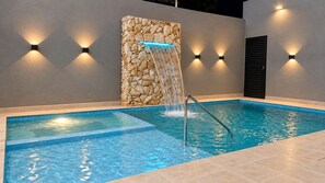 A swimming pool with a waterfall feature, surrounded by walls with built-in lighting.