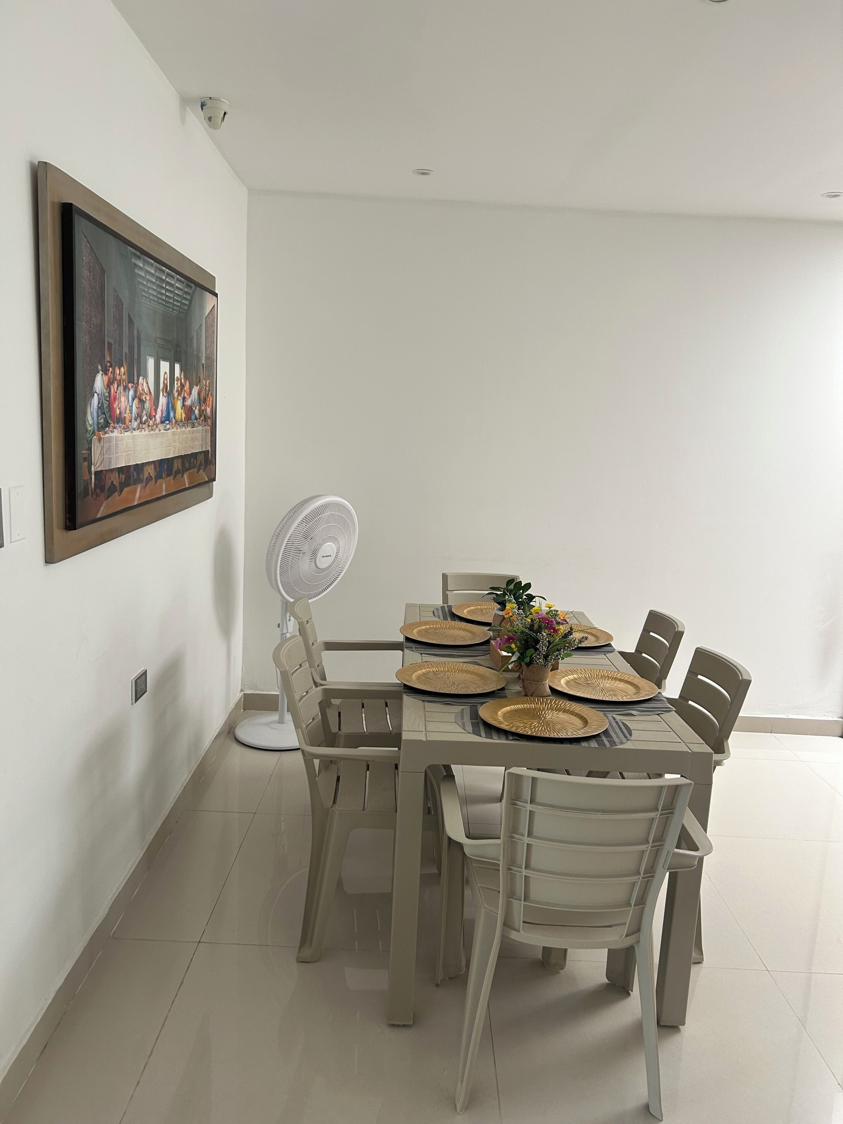 A dining area with a table set for four, surrounded by chairs, a ceiling fan, and a painting on the wall.