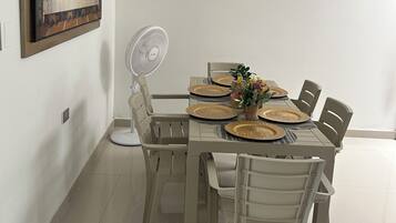 A dining area with a table set for four, surrounded by chairs, a ceiling fan, and a painting on the wall.