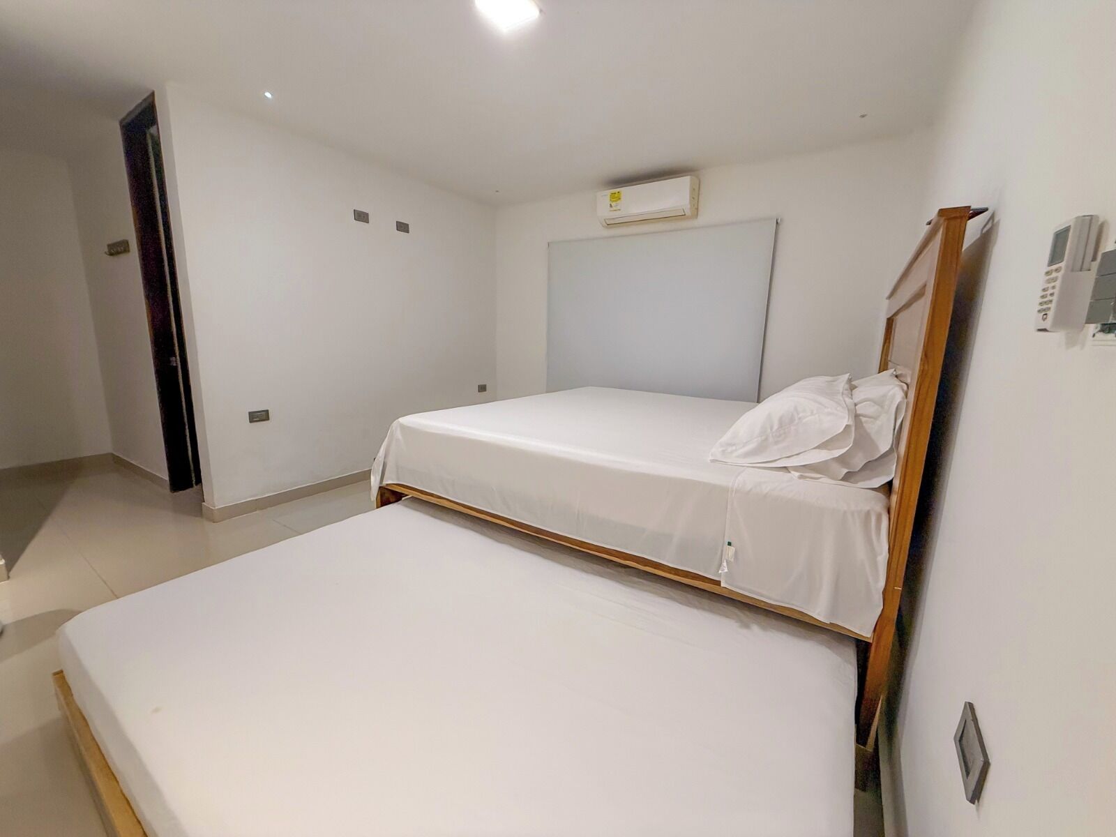 A room with two beds, a door, and an air conditioning unit on the wall.
