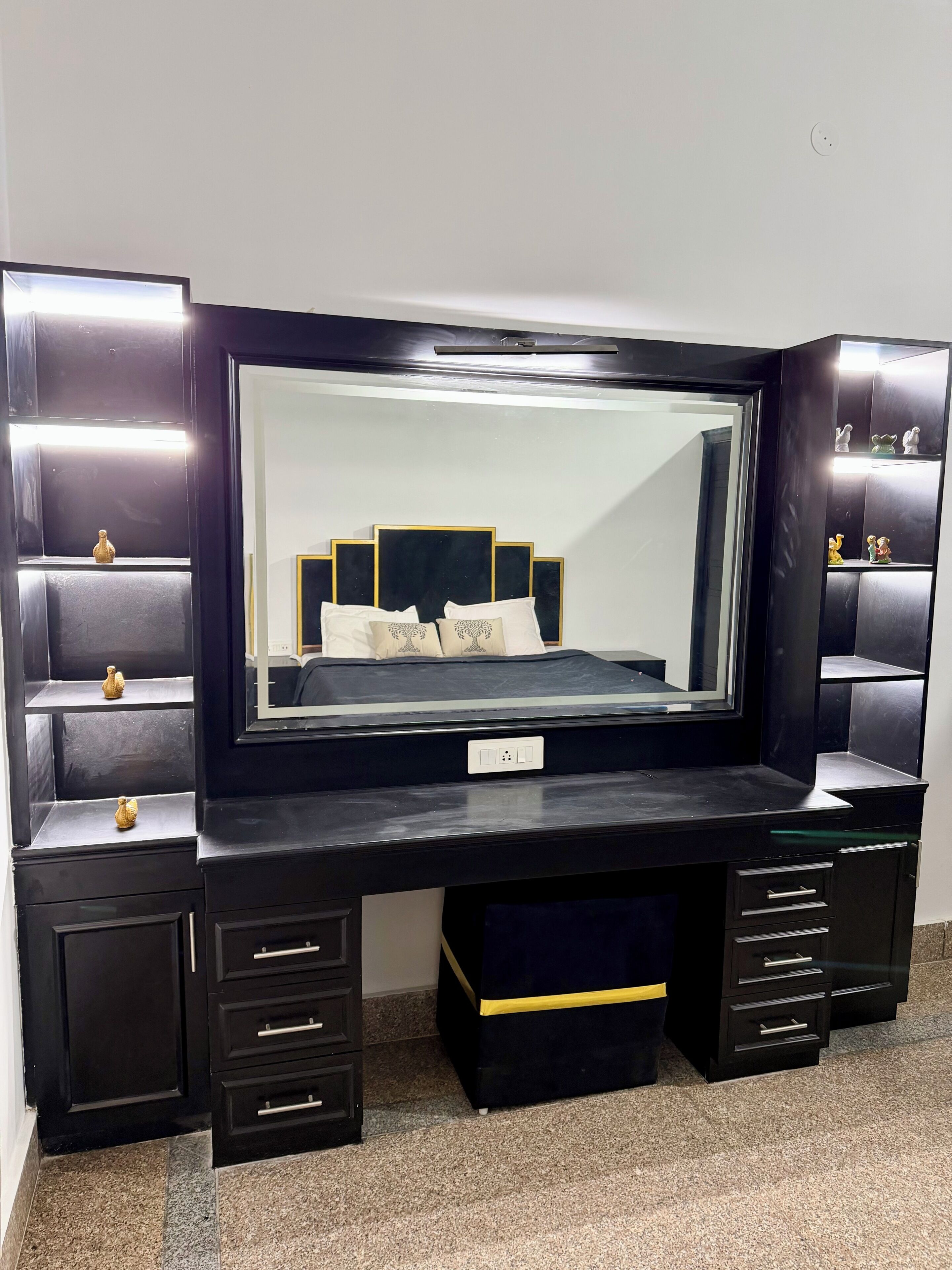 A black vanity with a large mirror, multiple drawers, and a shelf with decorative items.