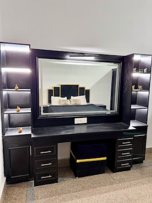 A black vanity with a large mirror, multiple drawers, and a shelf with decorative items.