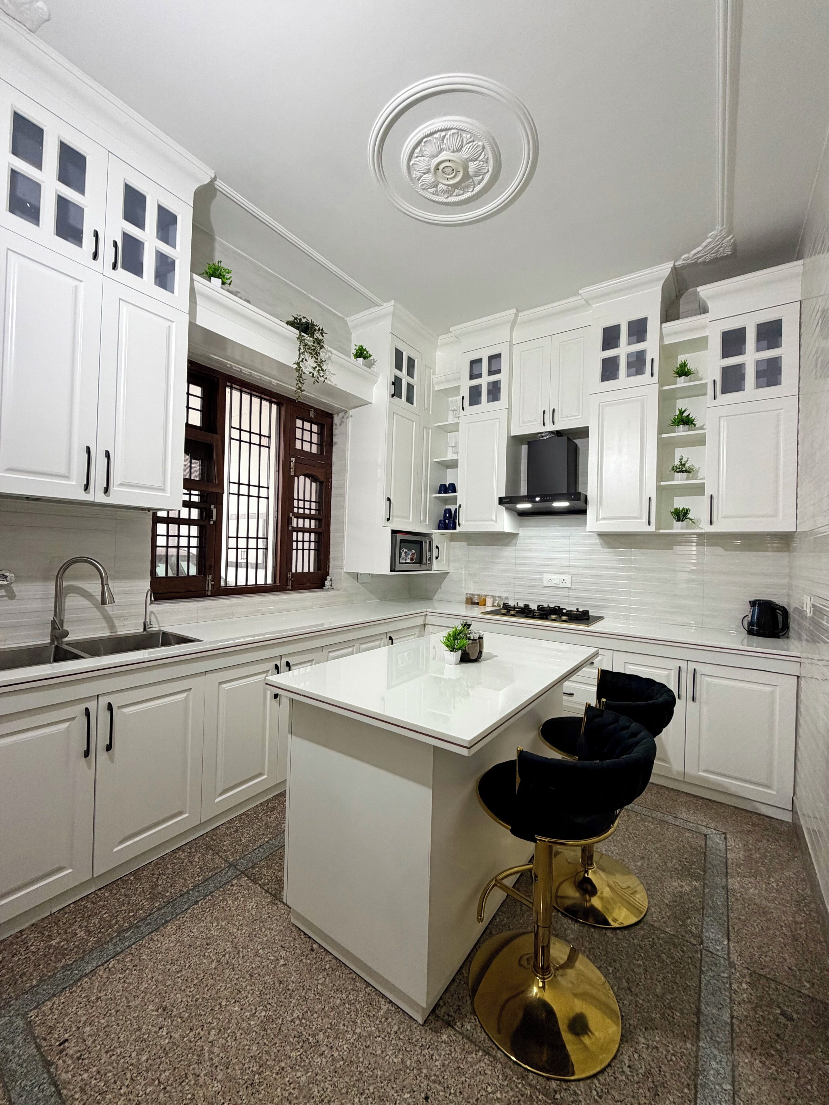 Een moderne keuken met witte kasten, een centraal eiland en een zwarte barstoel.
