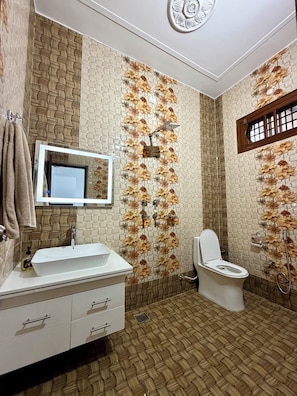 Une salle de bain avec un lavabo blanc, un miroir et des toilettes. Les murs sont recouverts d’un motif texturé orné de motifs floraux.