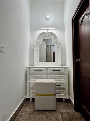 A white vanity with a mirror, a small stool, and a door to the right.