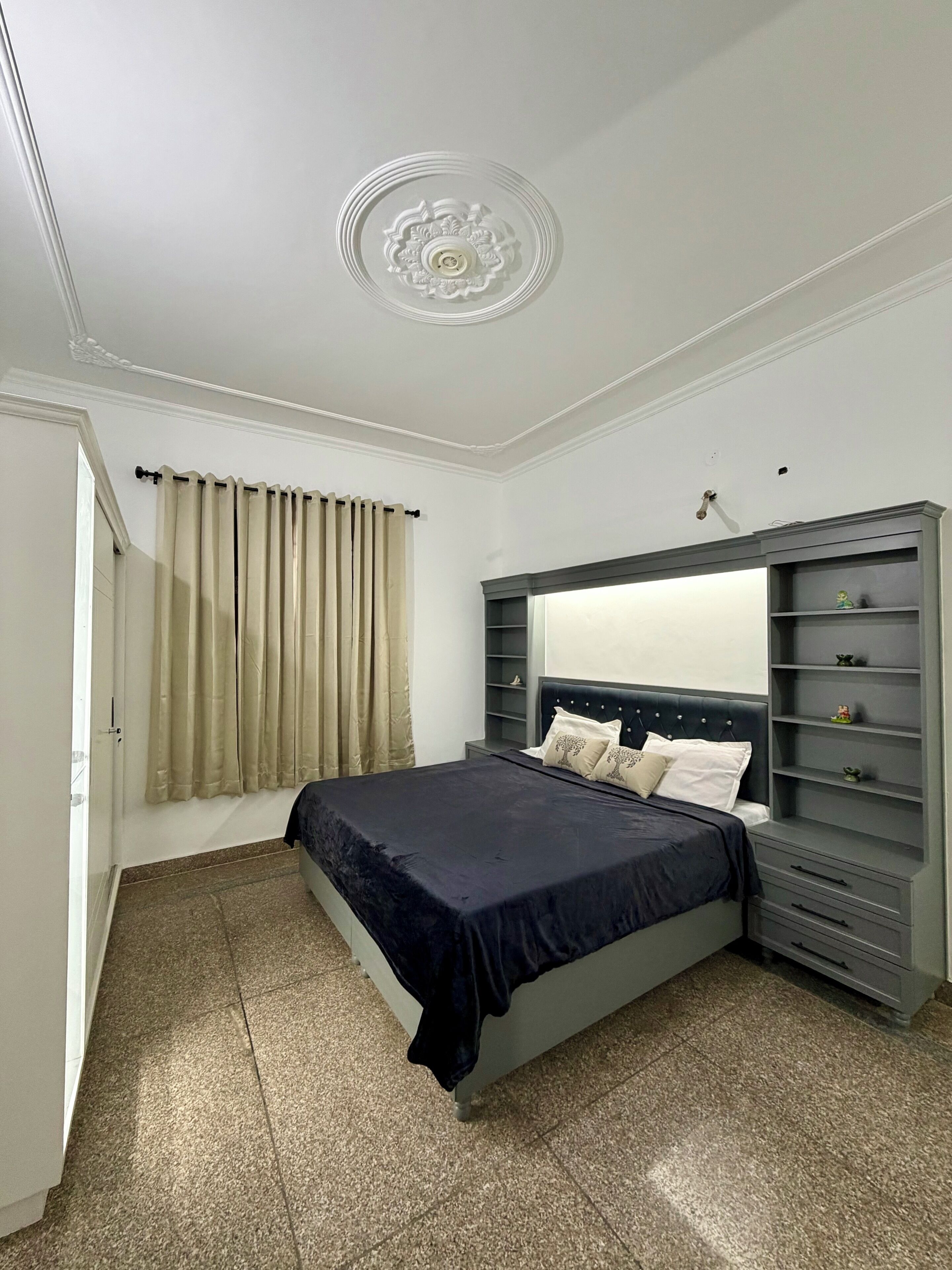 Une chambre à coucher avec un lit, une table de chevet, une commode, un miroir et une fenêtre avec des rideaux.