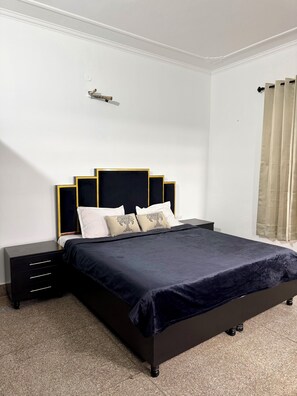 A modern bedroom with a dark blue bed, white pillows, and a black nightstand with drawers.
