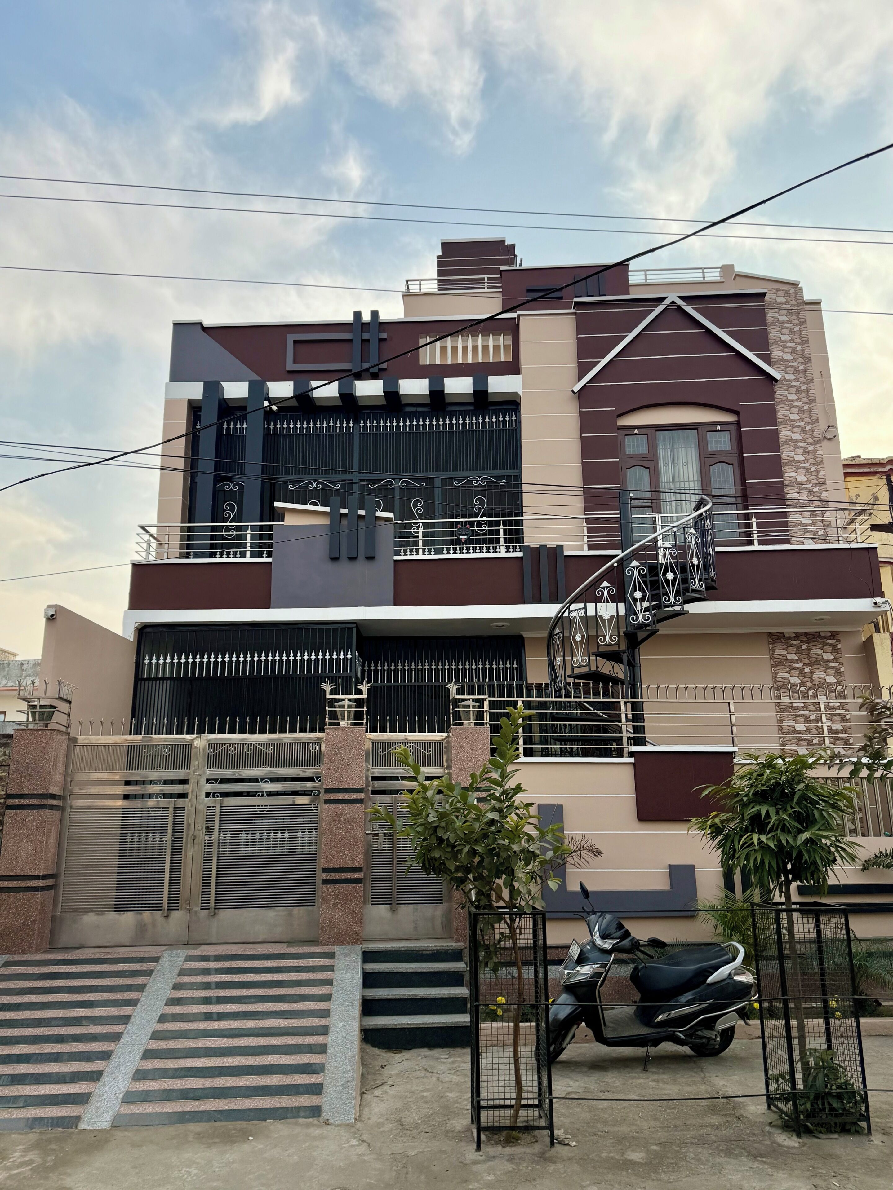 Une maison moderne à deux étages, dotée d’une entrée sécurisée par un portail, d’un escalier menant à l’étage supérieur et d’un scooter garé.