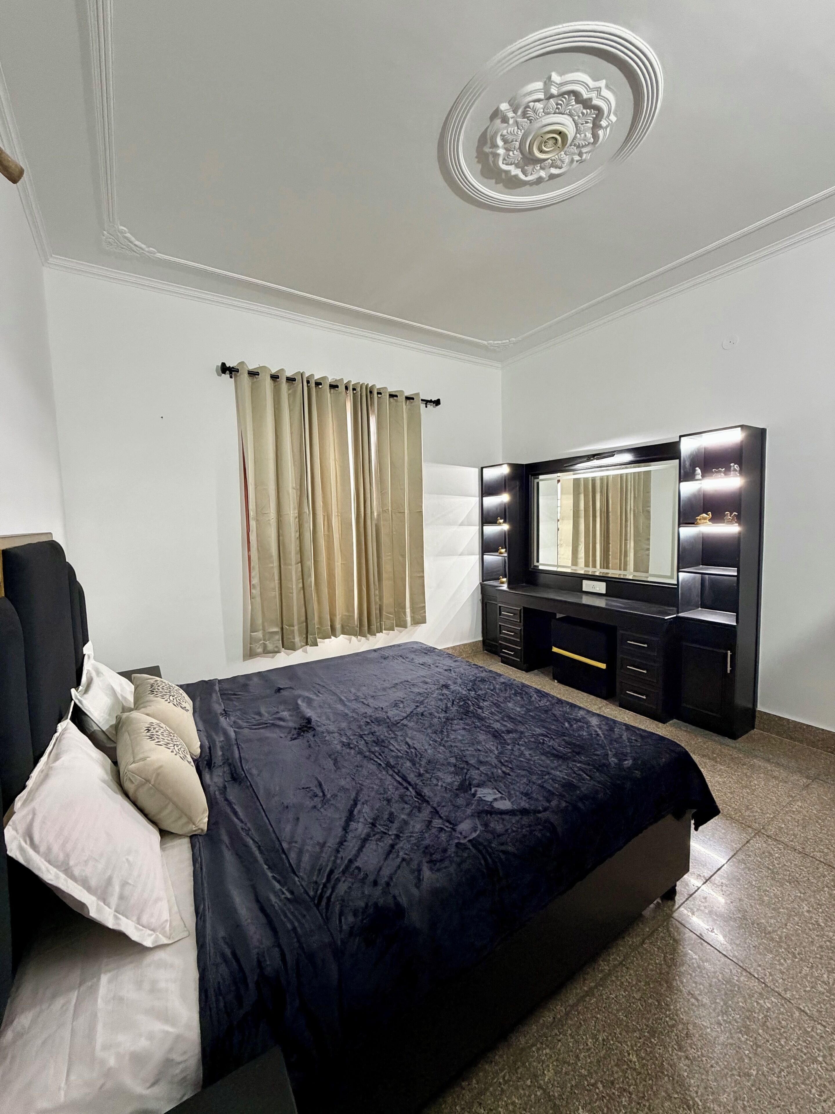 Une chambre à coucher comprenant un lit, une commode, une coiffeuse avec un miroir et un plafond orné d’un motif décoratif.