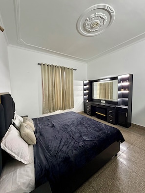 Une chambre à coucher comprenant un lit, une commode, une coiffeuse avec un miroir et un plafond orné d’un motif décoratif.