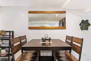 A dining area with a wooden table, chairs, a mirror, and a decorative wall piece.