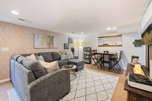 A modern living room with a sectional sofa, a coffee table, and a dining area with a table and chairs. - *New* Gorgeous Open Space, Perfect Location, Private Apartment! (Millcreek)
