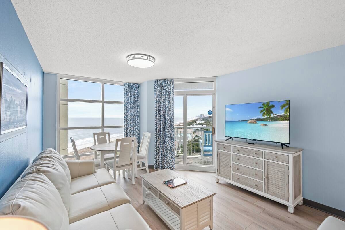 A living room with a sofa, chairs, a coffee table, a TV, and a view of the ocean.