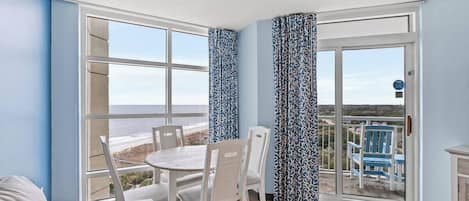 Una habitación con una mesa de comedor y sillas, un sofá, y vistas a la playa a través de amplios ventanales.