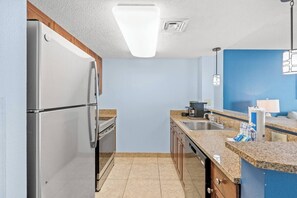 A kitchen with a stainless steel refrigerator, a built-in oven, a granite countertop, and a blue accent wall. - DunesVillage Resort & Waterpark! (Myrtle Beach)