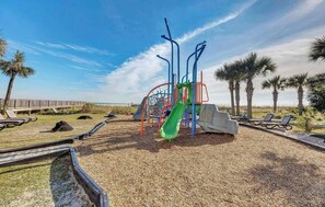 A playground with a slide, swings, and a wooden deck. - DunesVillage Resort & Waterpark! (Myrtle Beach)