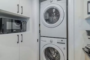 A compact laundry area with a top-loading washing machine and a front-loading dryer. - The Champlain | Rooftop pool BBQ| AC (Québec)