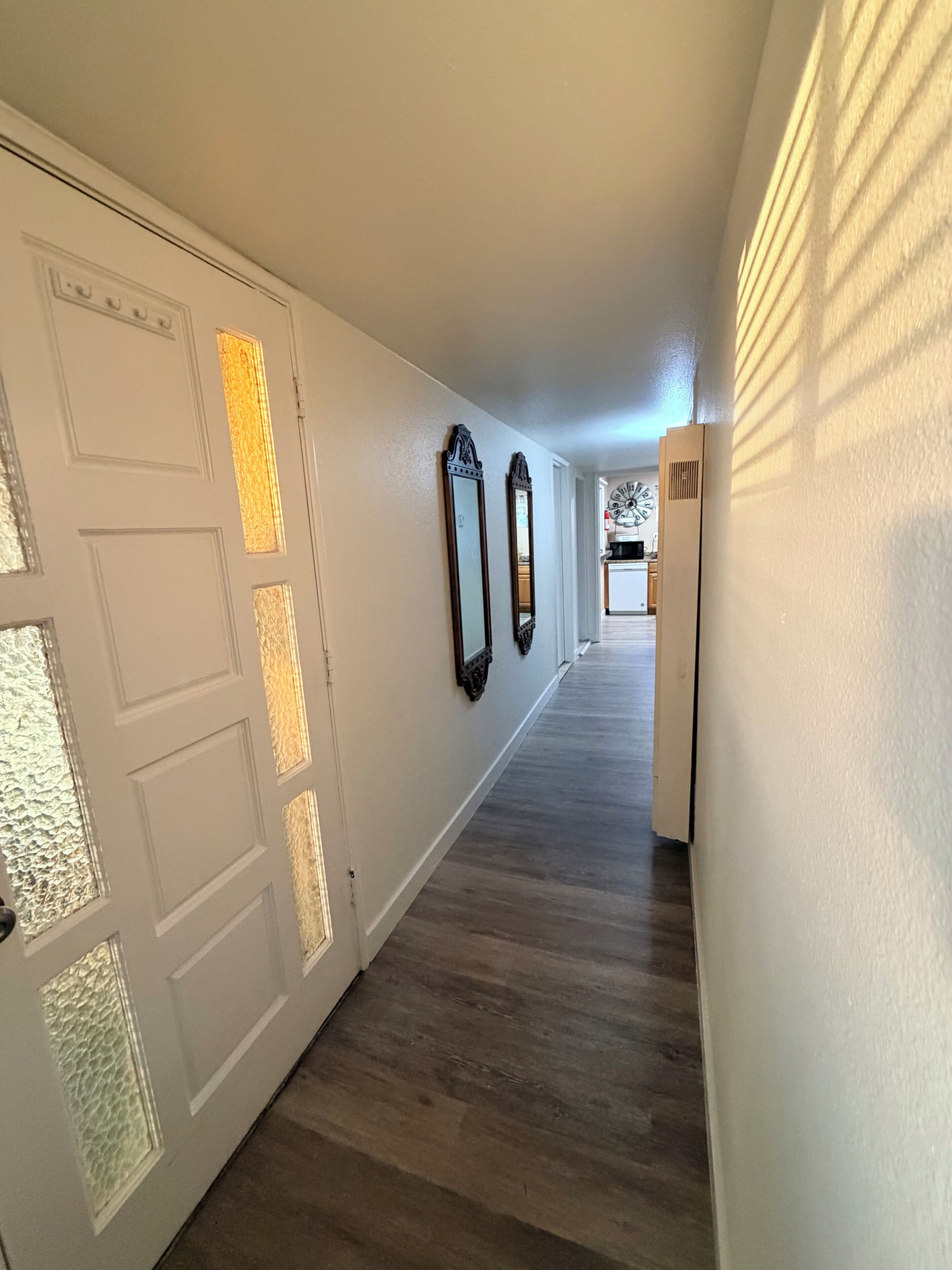 A hallway with a wooden floor, white walls, and a door with frosted glass panels.