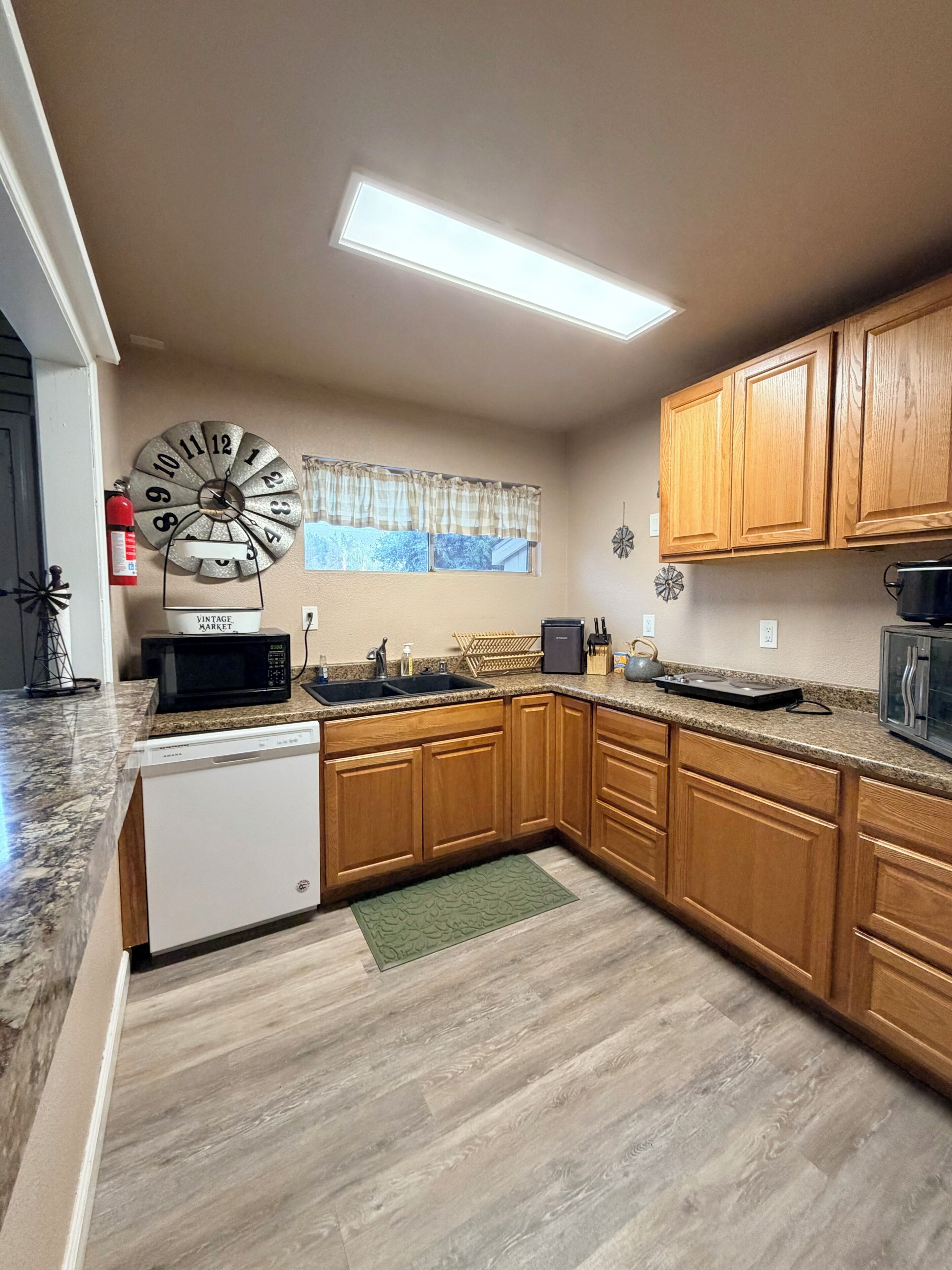 A kitchen with wooden cabinets, a microwave, a sink, and a clock on the wall.