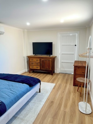 Ein Schlafzimmer mit einem Bett, einer Holzkommode, einem Fernseher und einer Tür.