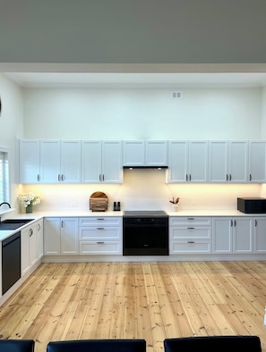 A modern kitchen with white cabinets, a black dishwasher, and a wooden floor.