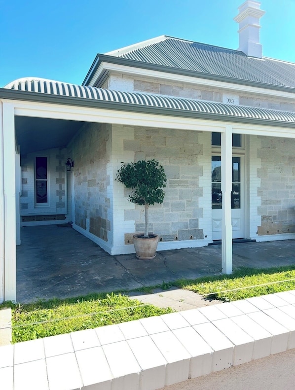 A covered porch with stone walls, a potted tree, and a clear sky.