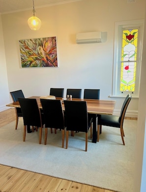 A dining room with a wooden table and black chairs, a hanging light fixture, an air conditioning unit, and a stained glass window.