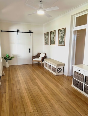Ein Zimmer mit Holzboden, Deckenventilator, einer Sitzbank, einem an der Wand befestigten Kasten und gerahmten Pflanzenbildern.
