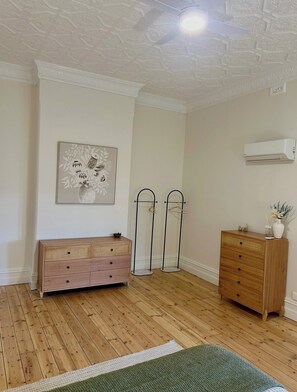 A room with a wooden floor, a dresser, a wall-mounted air conditioner, and a framed floral artwork.
