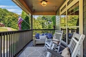 A covered porch with a wooden railing, a bench with cushions, and an American flag.