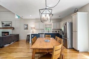 A modern kitchen with a dining area, wooden flooring, and a fireplace.